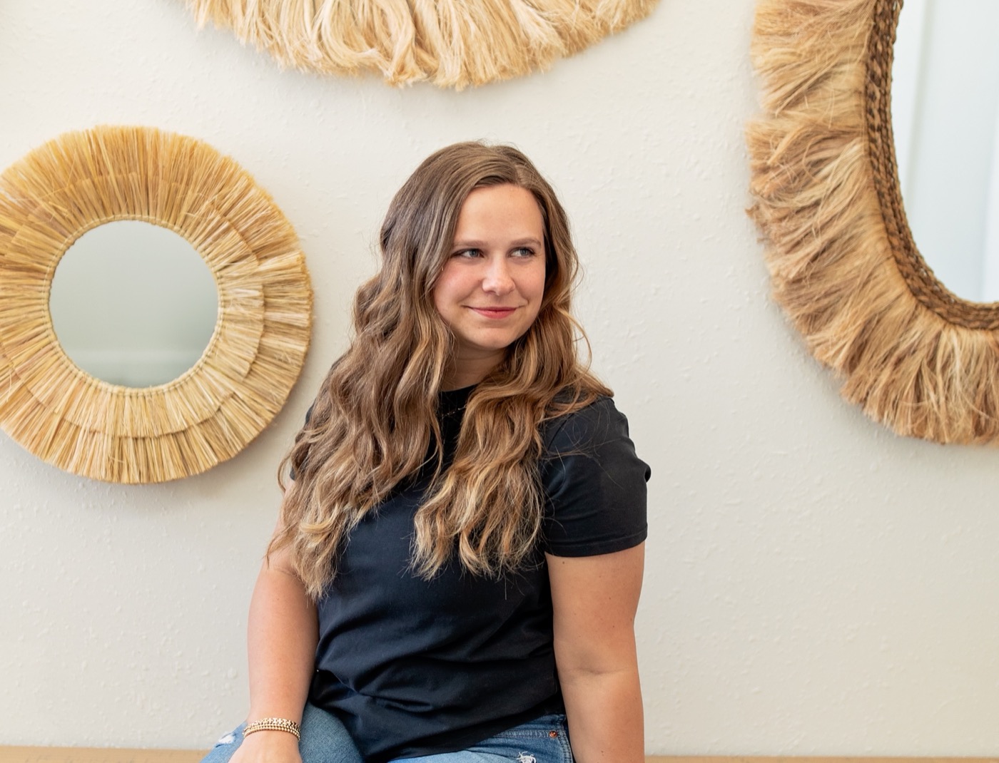 Marisa Grover in a black tee, sitting in front of woven wall mirrors