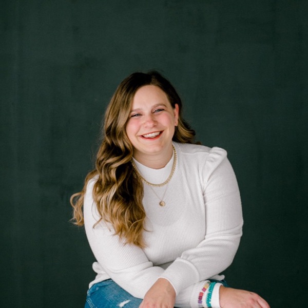 Marisa Grover smiling in a white sweater, sitting on a wooden stool