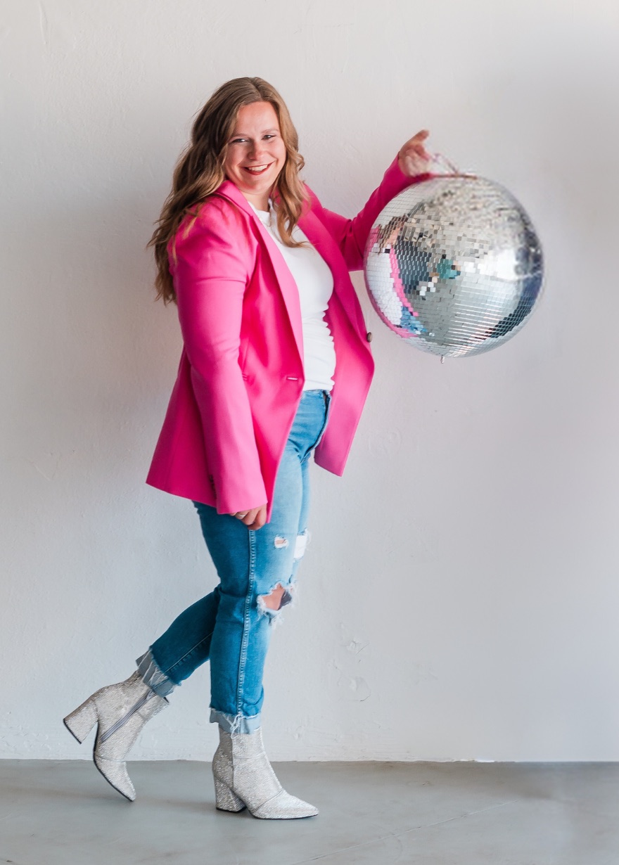 Marisa Grover in a pink blazer and sparkly boots, laughing and holding up a disco ball
