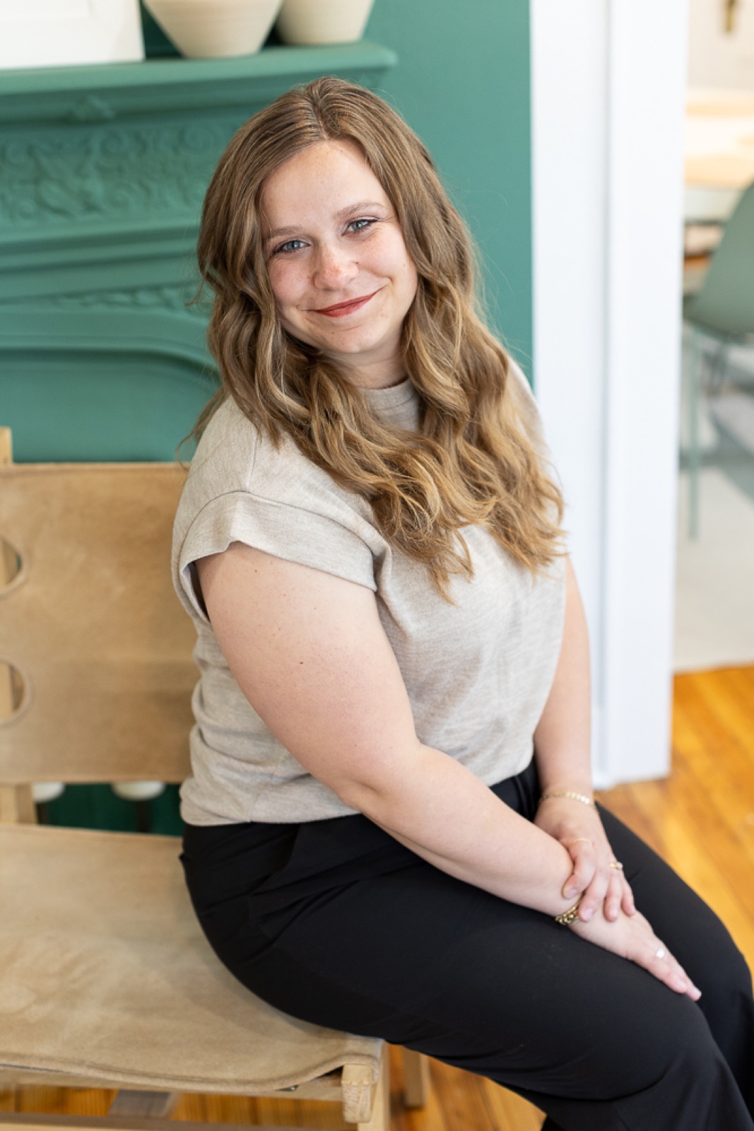 Marisa Grover smiling, sitting on a wooden chair in front of a green mantel